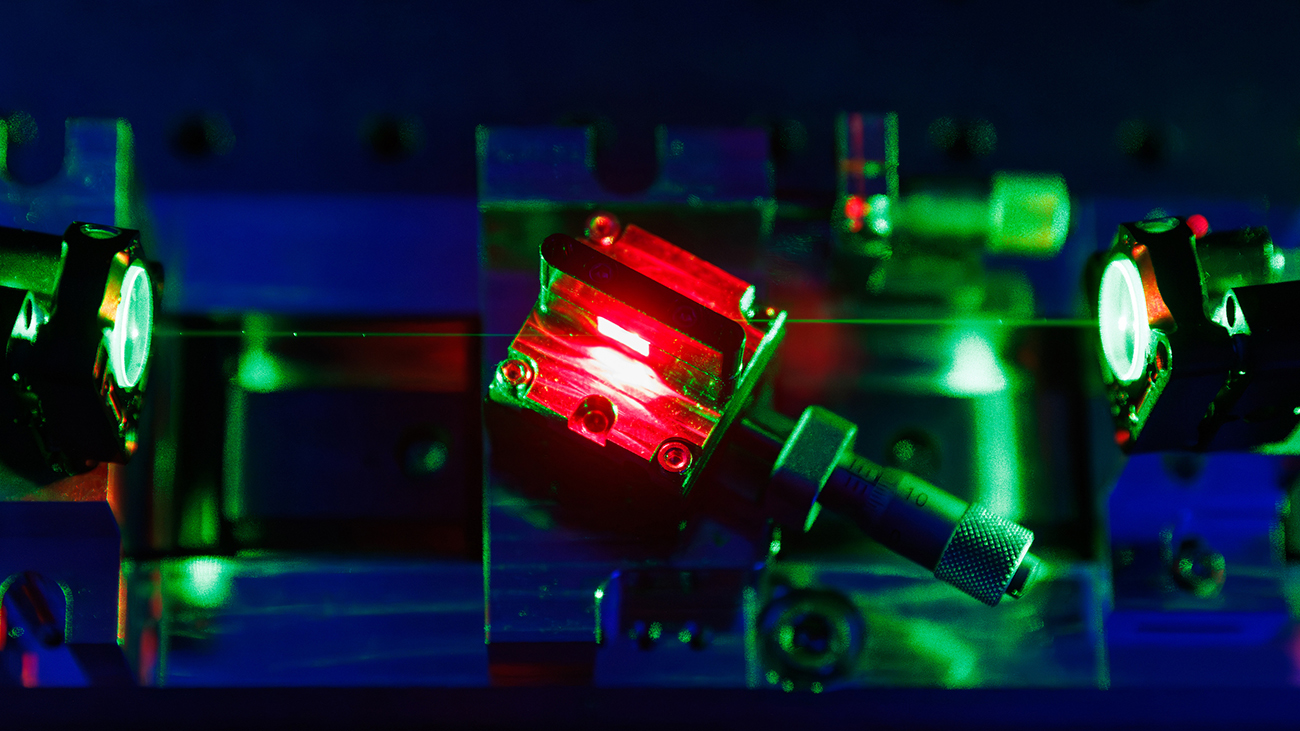 In a dark lab, a scientific device projects a green laser beam through a glowing red prism