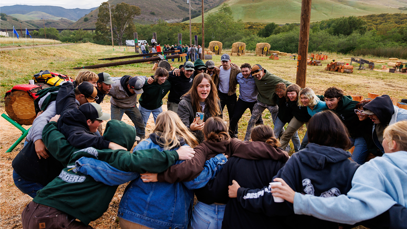 A group of Cal Poly students gather in a circle in a field