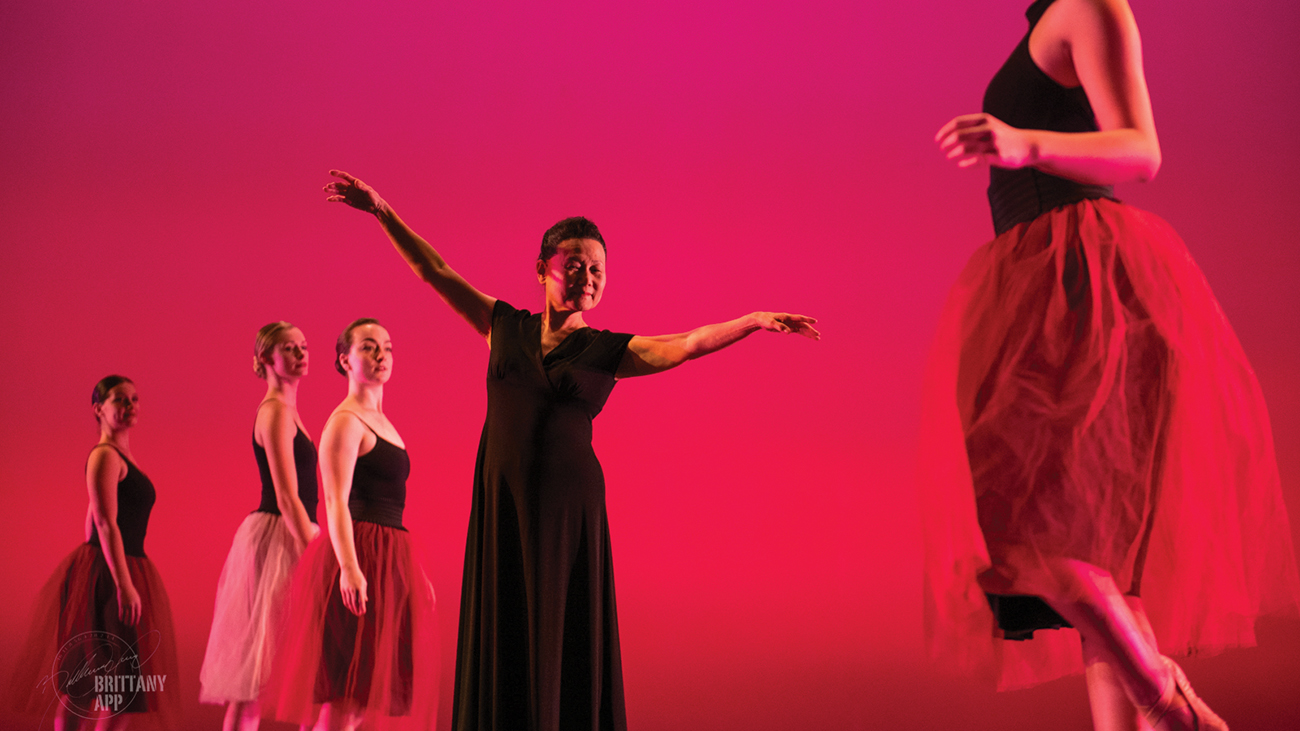 Dancers and emeritus professor Moon Ja Minn Suhr dance on stage before a red background