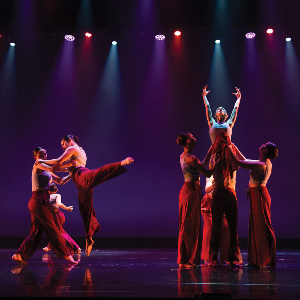 A group of Orchesis dancers perform on stage under dramatic lighting