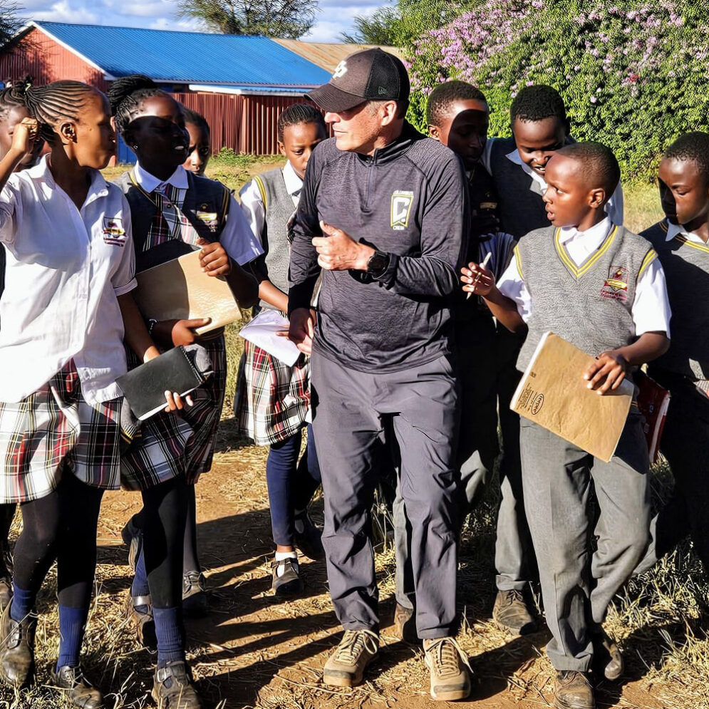 A man in a hat walks among a group of students in school uniforms