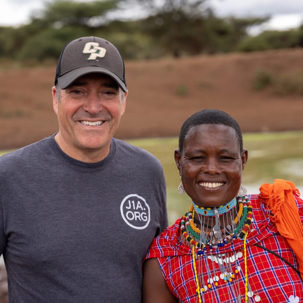 A man in a Cal Poly hat poses with a person in traditional jewelry and dress during a trip with the Just One Africa organization