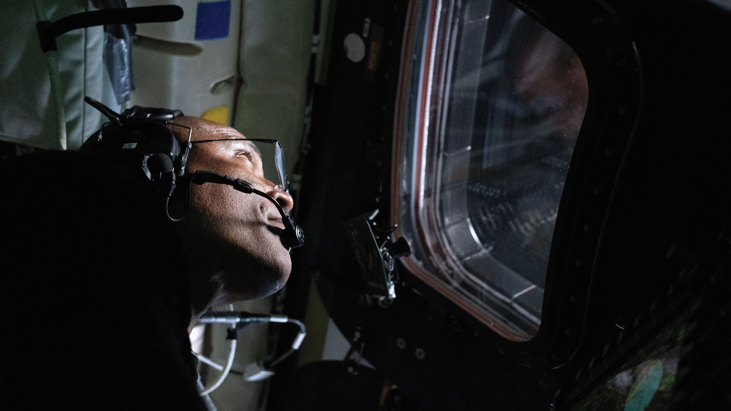 Astronaut Victor Glover wears a head set and looks out the window of the Orion capsule during the Artemis II lunar mission