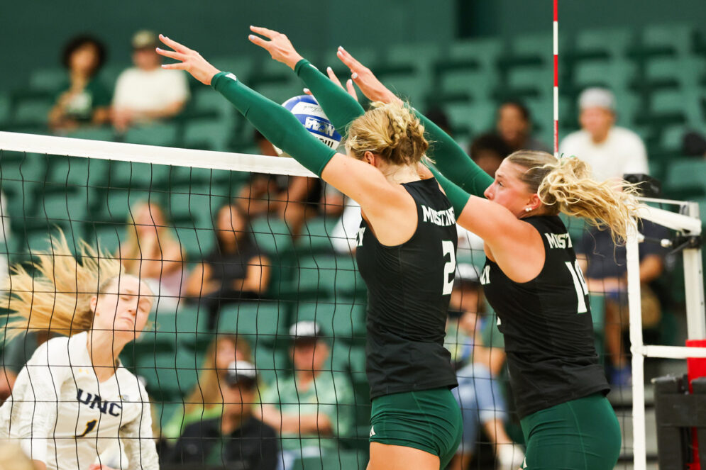 Two Cal Poly volleyball players block the ball from an opposing player in Mott Gym
