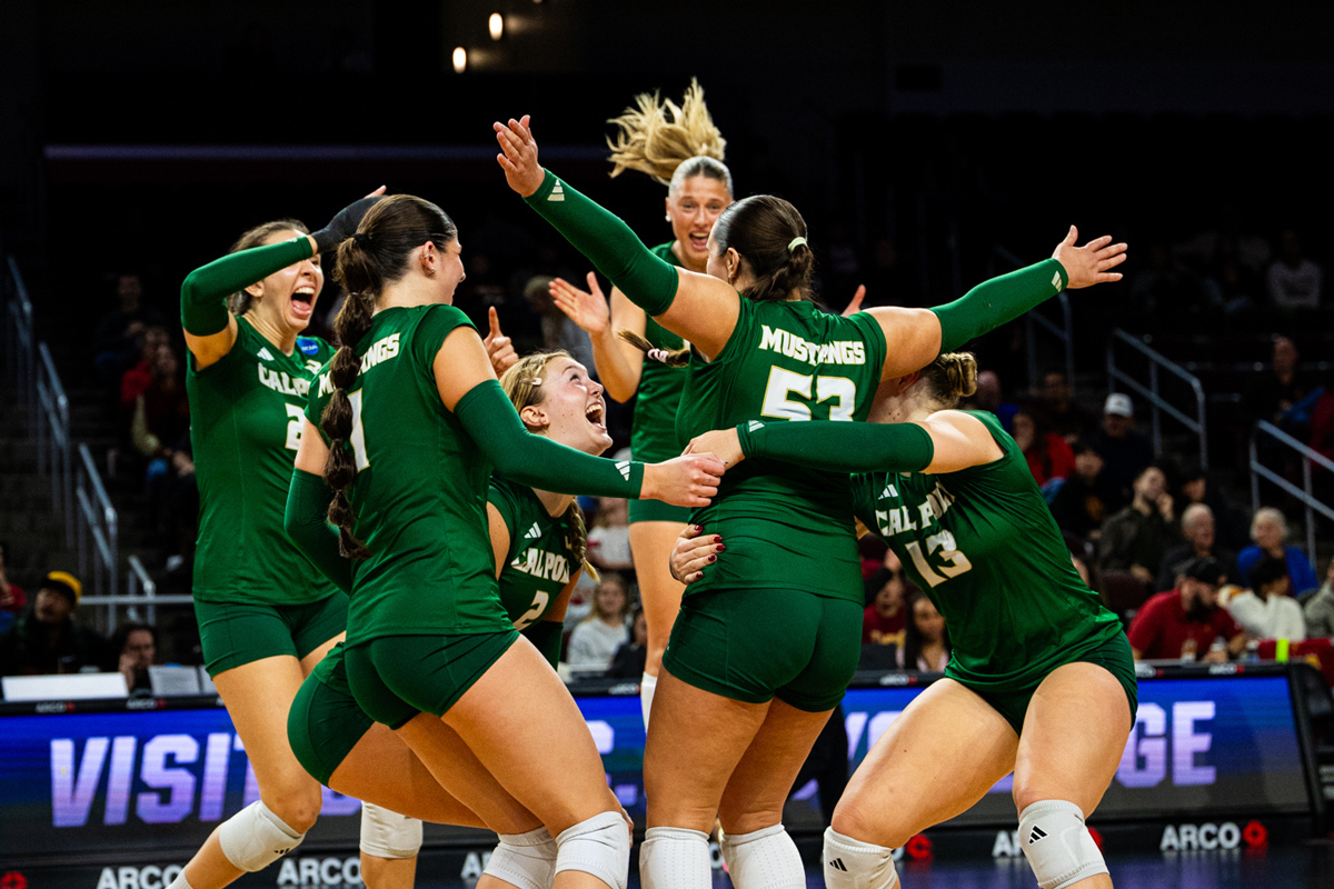 The Cal Poly volleyball team celebrates on the court wearing green uniforms