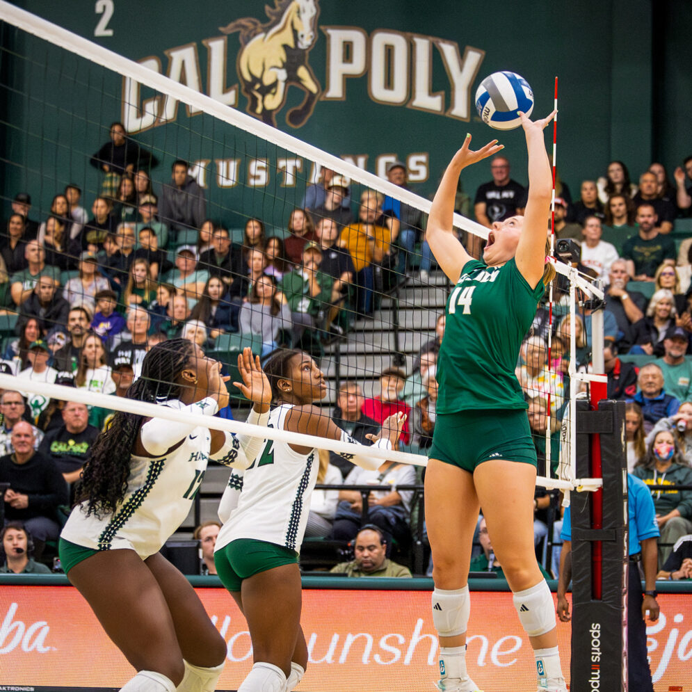 A Cal Poly Volleyball player sets the ball across the net from two defenders