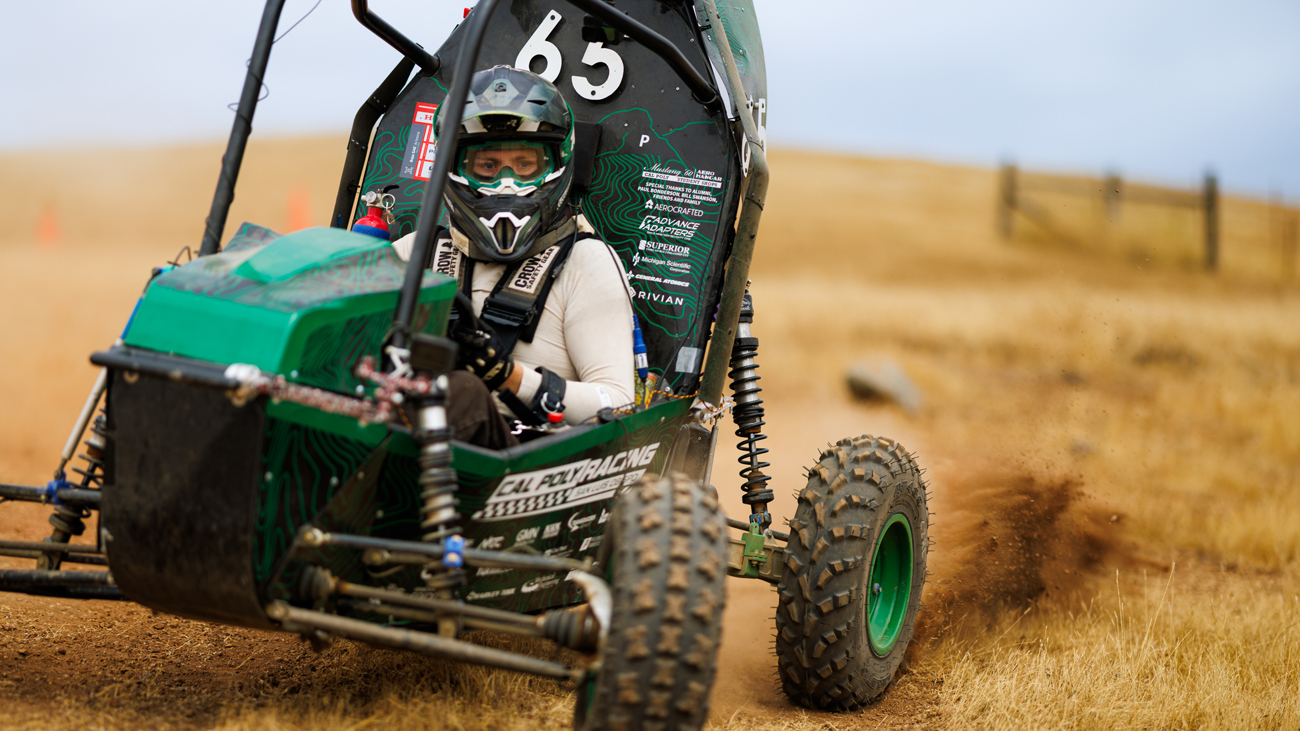 A driver pilots the Cal Poly Racing Baja car on a dirt test track