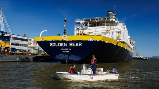 Cadets traveling in a small boat in front of the Training Ship Golden Bear.