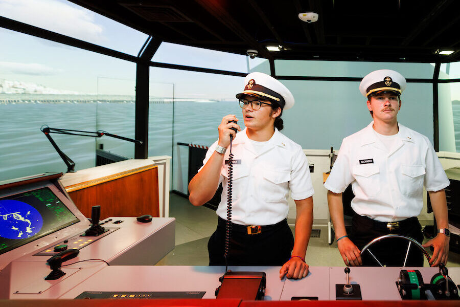 Two students in black and white uniforms work on Cal Poly Maritime Academy's bridge simulator.