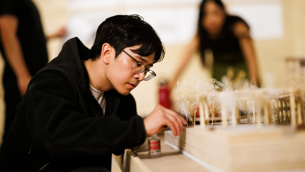 A young man carefully adjusts details on an architectural model