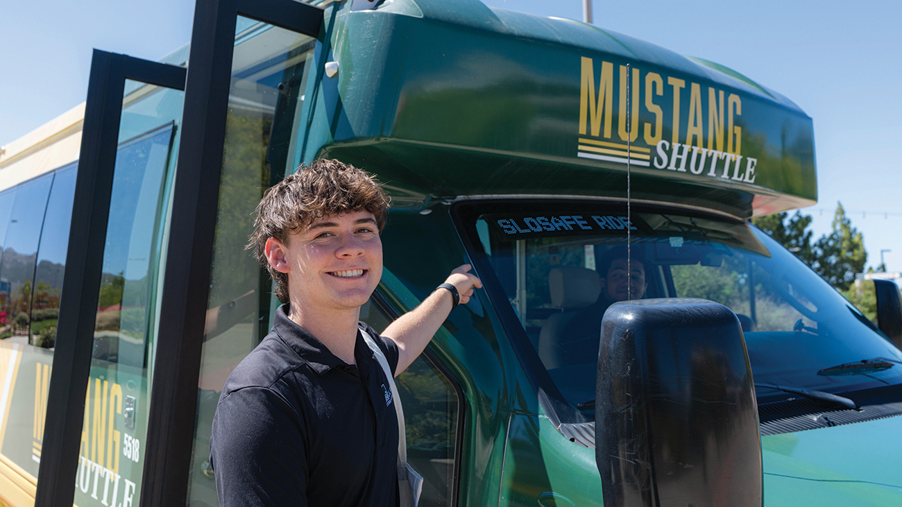A young man smiles in front of a green and gold bus.