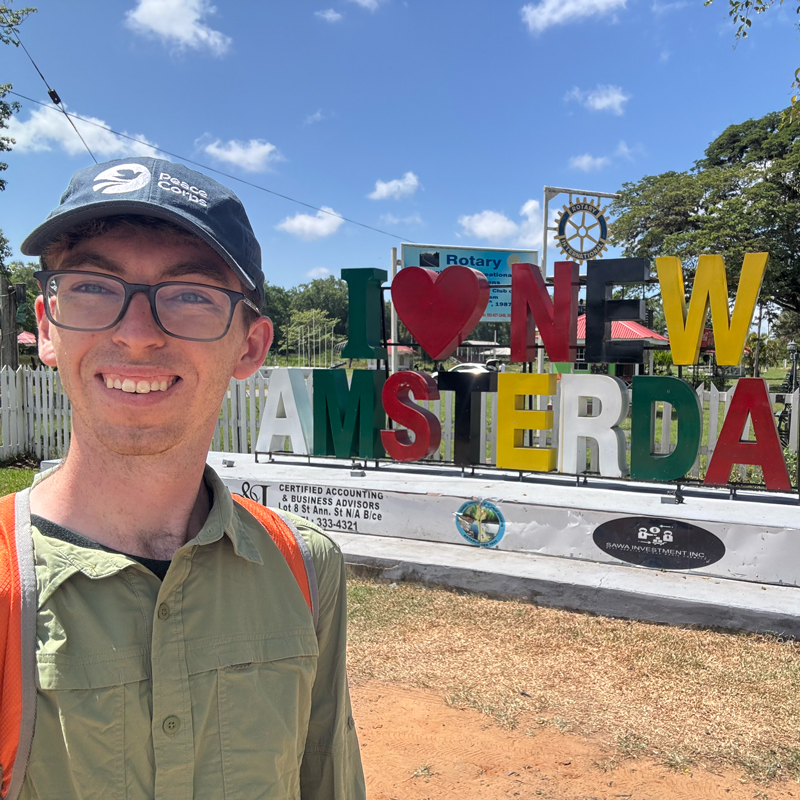 A student in a Peace Corps hat stands in front of a New Amsterdam sign