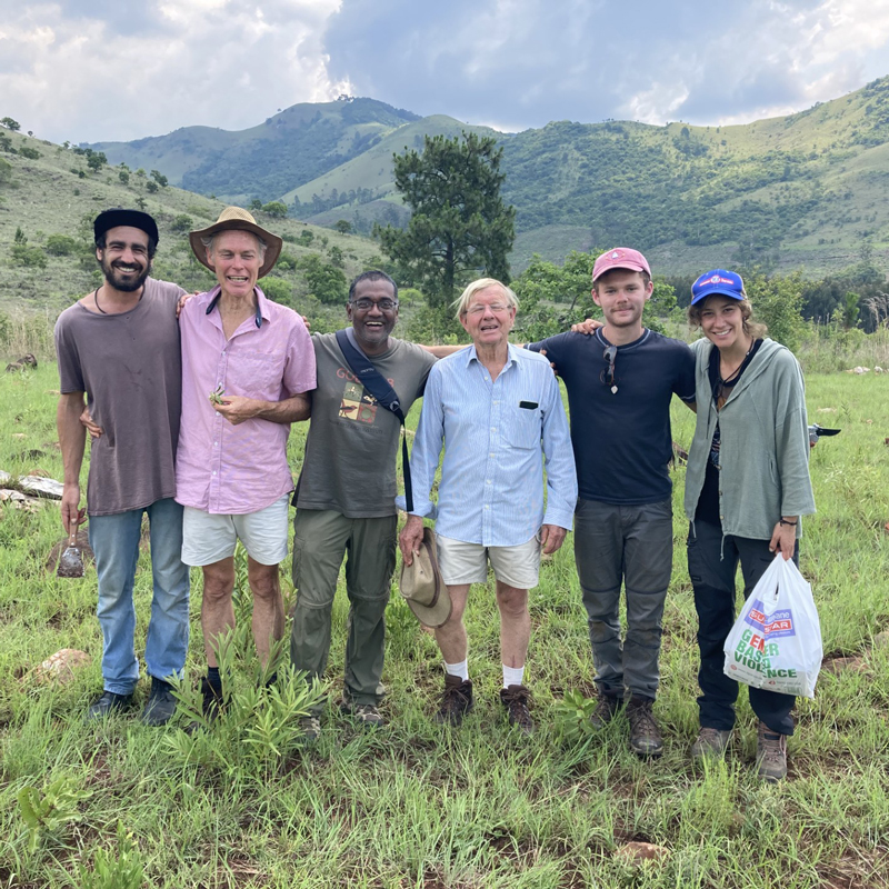 Six botanists stand before lush grass and hills behind them.