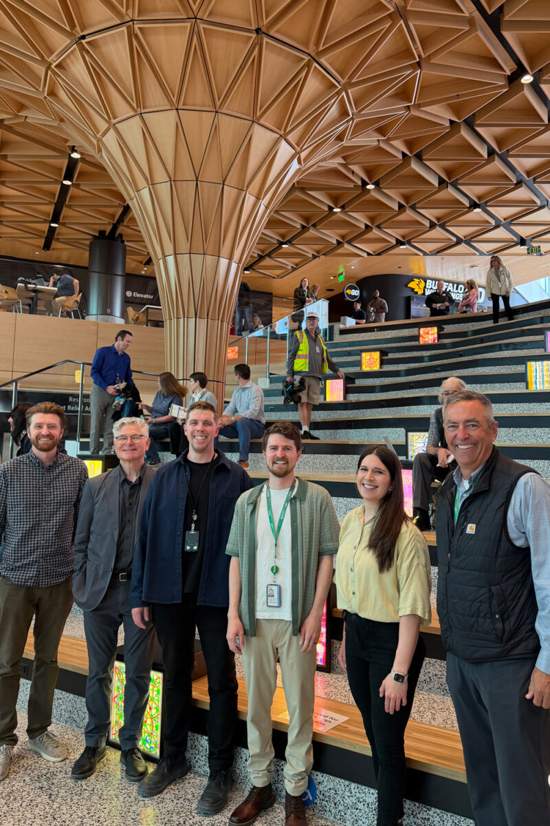 Six people stand in front of amphitheater seating and a geometric architecture structure