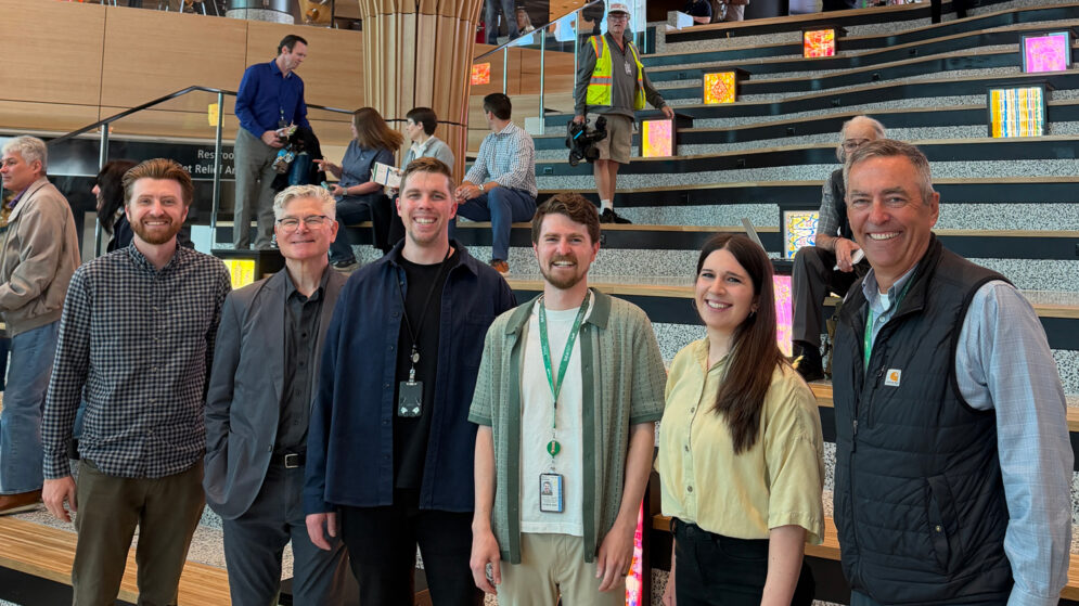 Six people smiling in front of an architectural installation