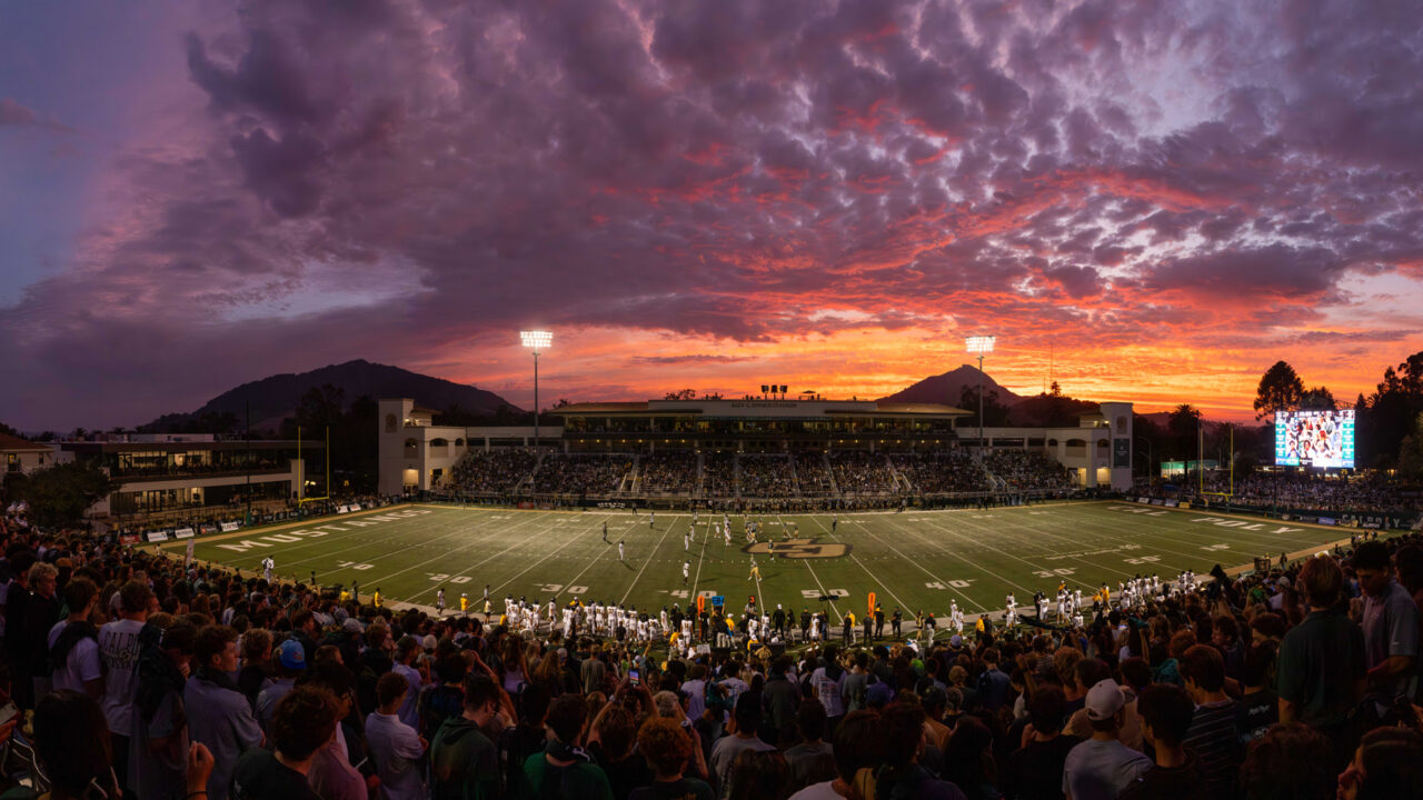 A colorful sunset colors the sky above a Cal Poly football game in Spanos Stadium.