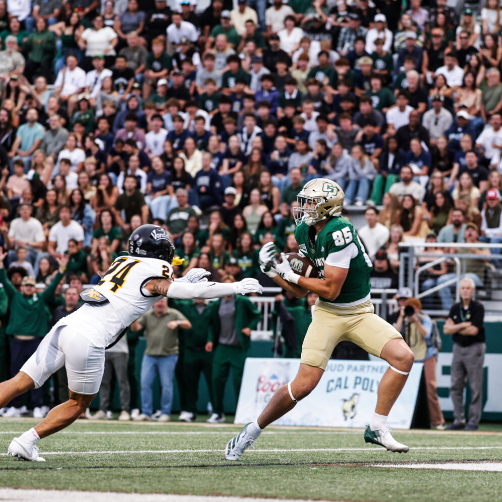 A Cal Poly football player catches a pass in the end zone in front of a packed stadium.