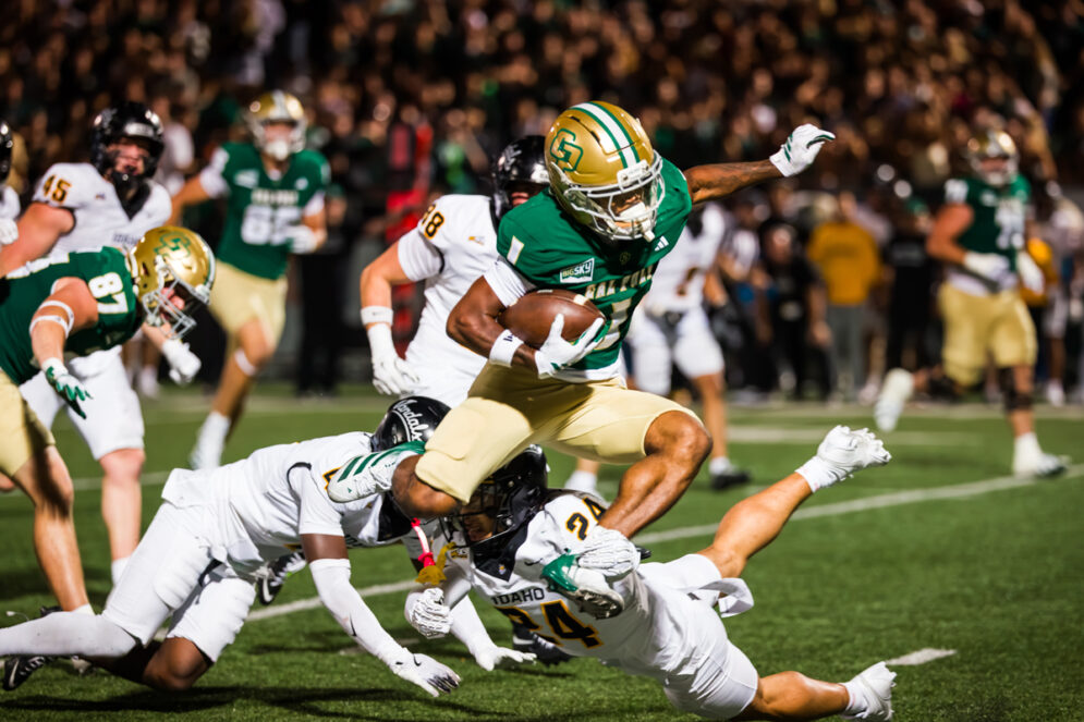 A running back carries the ball while jumping over defenders during a football game