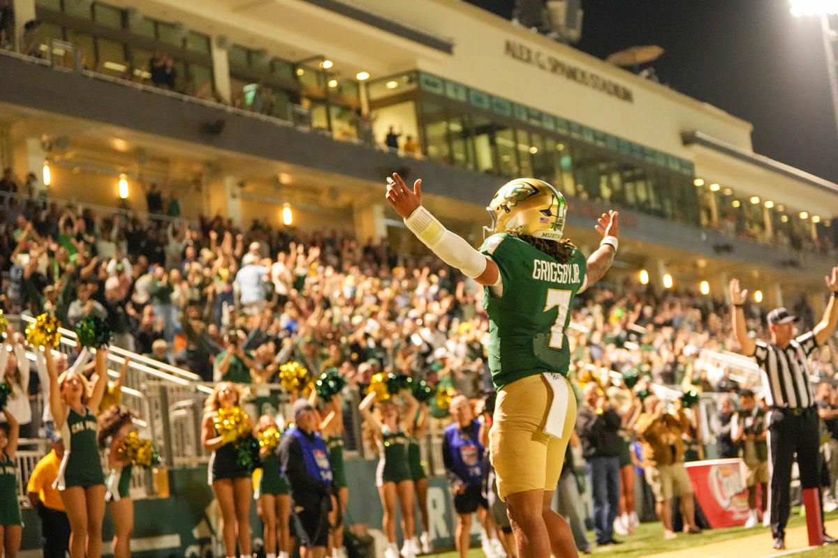 A Cal Poly football player raises his arms in celebration in front of a stadium of cheering fans.