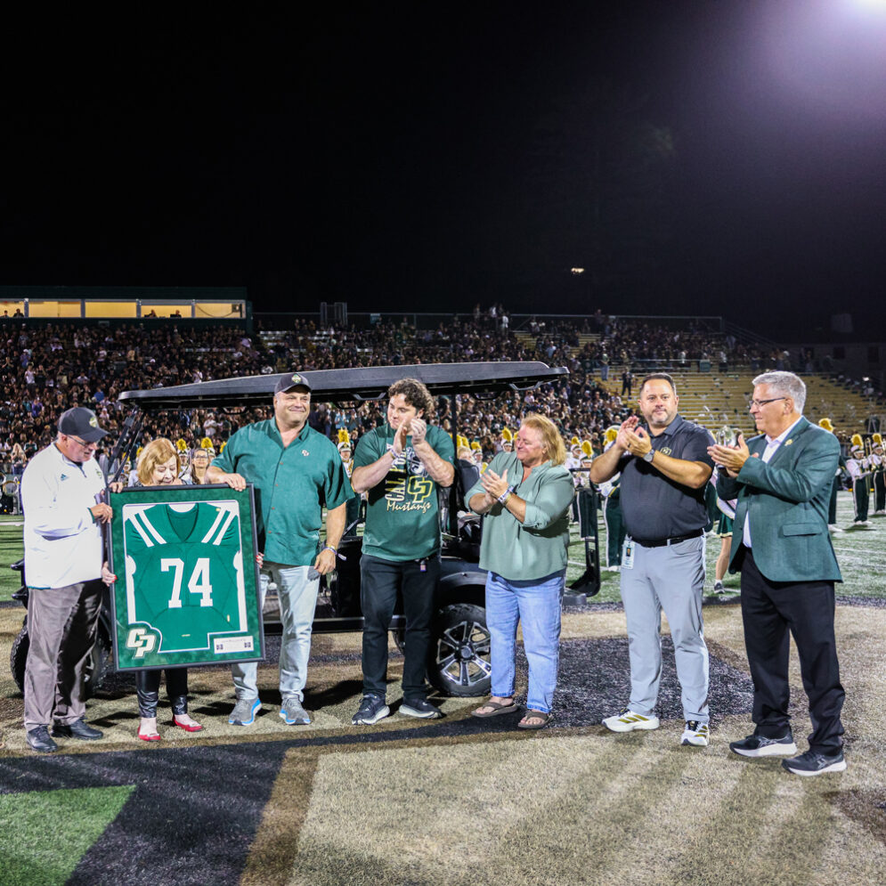 Five members of the Madden family stand at midfield in Spanos Stadium with two Cal Poly administrators while holding a green jersey with the number 74.