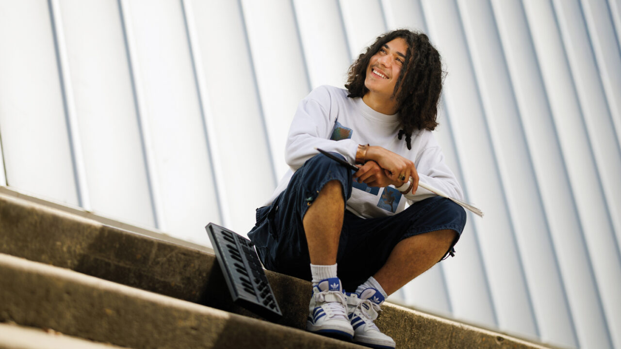 A student sits outside Phillips Hall with a keyboard