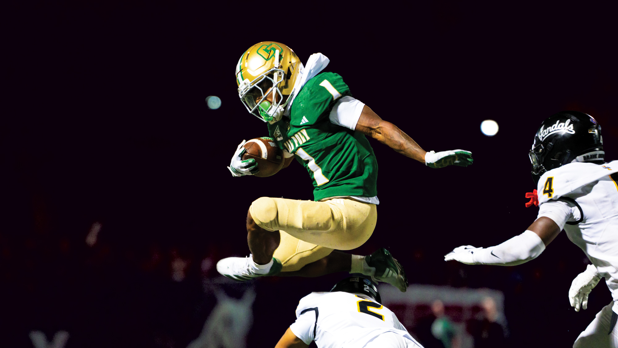 A Cal Poly football player jumps over a diving defender during a game in Spanos Stadium.