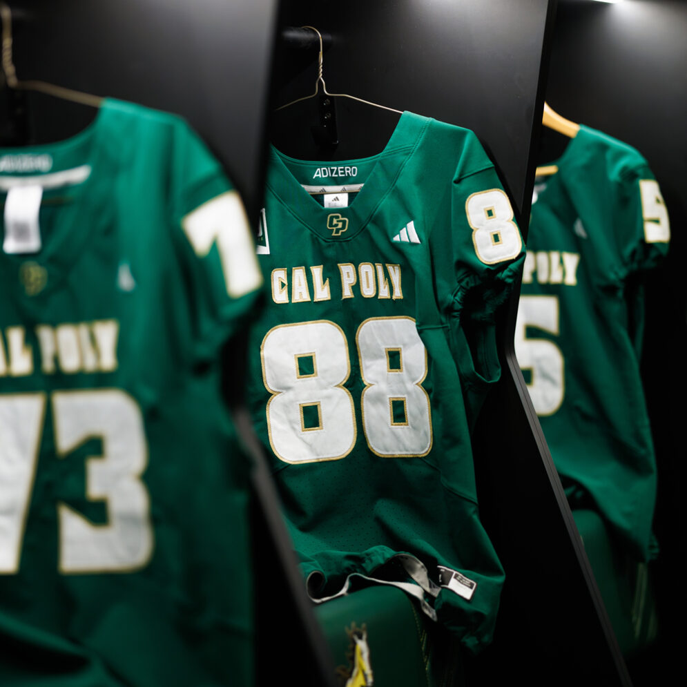 Three green Cal Poly football jerseys hang in lockers.