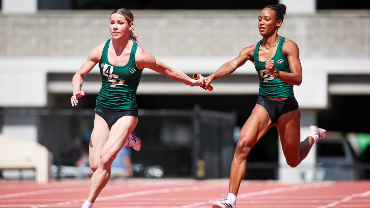 Two Cal Poly track athletes exchange the baton during a relay race.