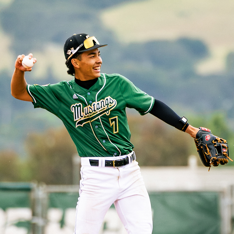 A baseball player in a green jersey prepares to throw a baseball on the infield
