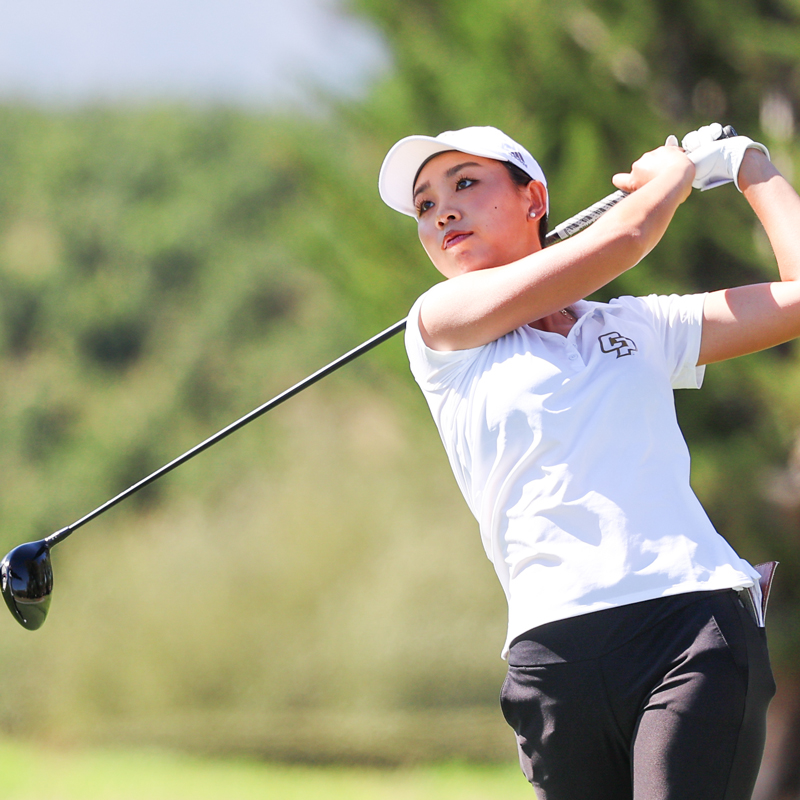 A Cal Poly women's golf team athlete swings the club and looks toward the ball