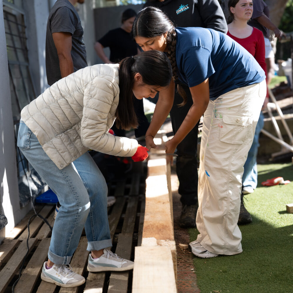 Two students work with a plank of wood in a construction area