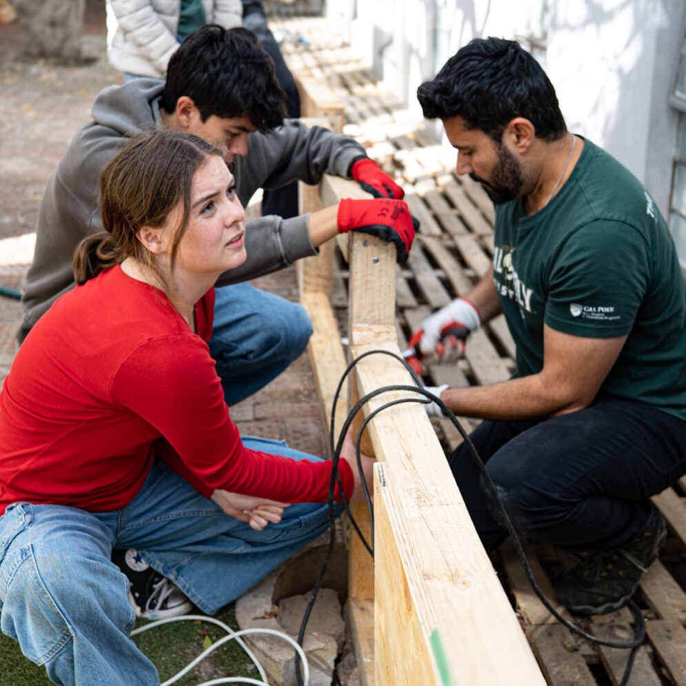 Three students work together using tools and wooden beams