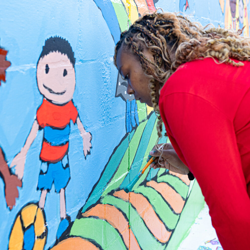 A student in a red sweater paints a colorful mural on a wall