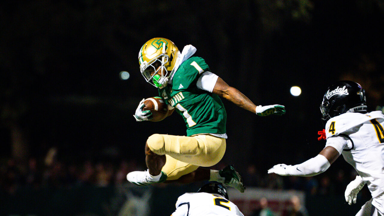 A Cal Poly football player jumping with the ball over an opponent.