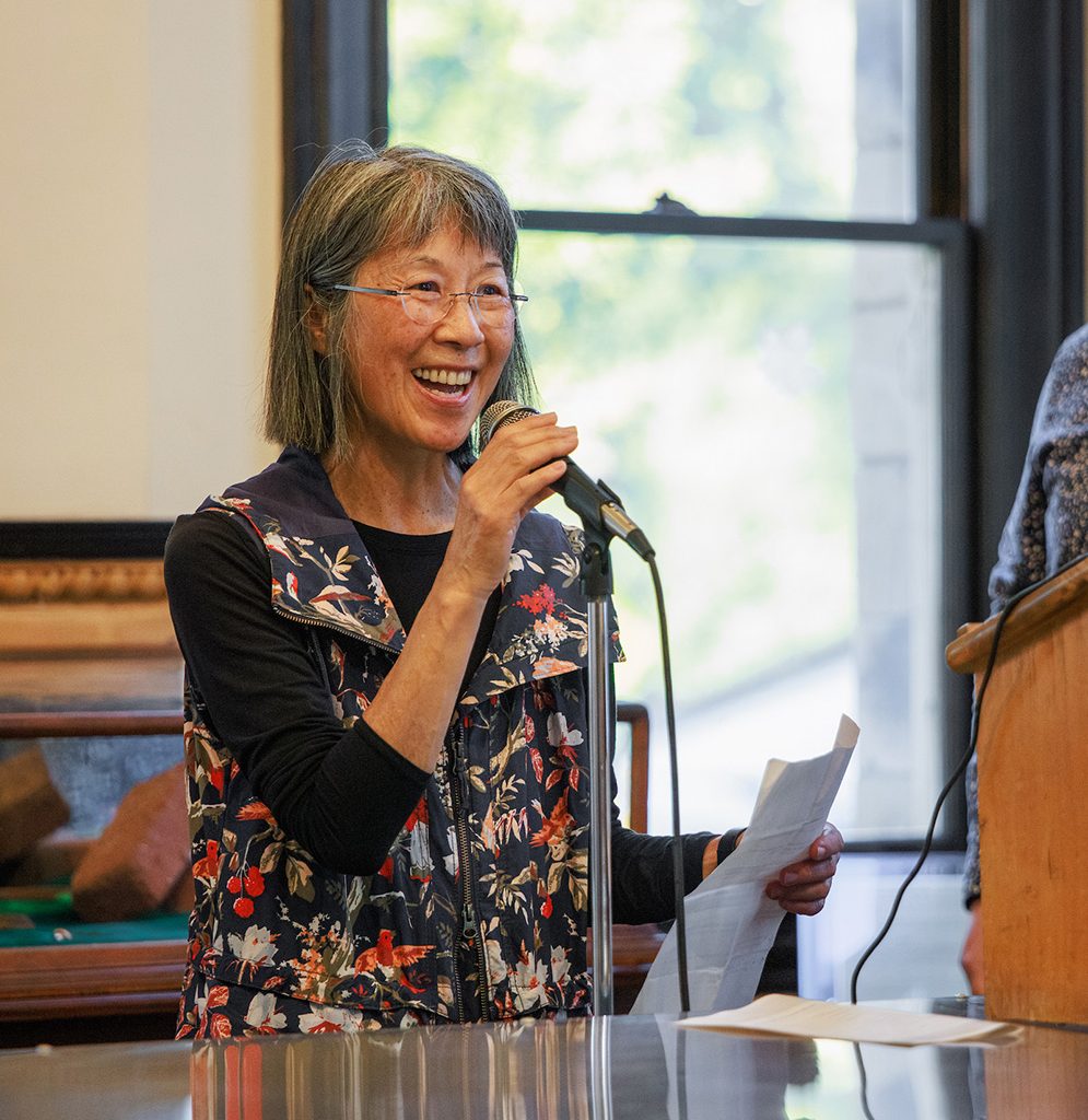 A Yoshida family member speaks using a microphone at a historical exhibit